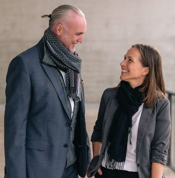 Volker Loibl und Melanie Reuß von apollo consulting im Gespräch vor einer Betonwand